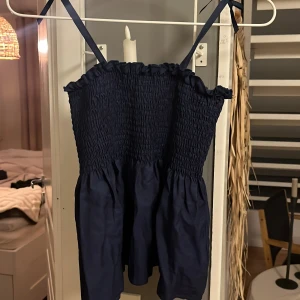 Mörkblå smockad linnetopp med rosett - Supersöt mörkblå linnetopp med smockad överdel och volangig nederdel. Oanvänd och inga slitna delar.