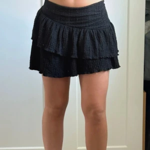 Svart volangkjol i bomull - Supersöt svart kortkjol med två lager volanger. Kjolen är gjord i ett strukturerat bomullstyg. Älskar denna kjolen men den är lite liten på mig. Aldrig använd! Storlek XS