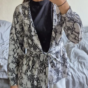 Overshirt med ormmönster och knytband - Säljer en snygg overshirt med svartvitt ormmönster. Jackan har långa ärmar med resår vid handlederna och ett knytband i midjan för en schysst passform. Perfekt att slänga över en t-shirt för en cool look.