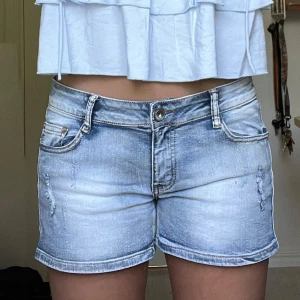Ljusblå jeansshorts - Snygga ljusblå jeansshorts från By Sasha i klassisk femficksmodell. De har slitna detaljer framtill med stenar på, uppvikta benslut och har en low/mid-waist passform💫 Midjemått: ca. 42 cm