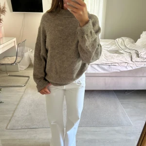 Beige stickad tröja med hög hals - Mysig beige stickad tröja med hög hals och avslappnad passform. Tröjan har långa ärmar och ribbade muddar vid hals, ärmslut och nederkant. 