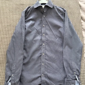 Mörkgrå skjorta från Stenströms Slimline - Snygg mörkgrå skjorta från Stenströms Slimline i bomull. Skjortan har klassisk krage, vita knappar och diskret mönstrat tyg på insidan av manschetterna. Passformen är slim och materialet känns mjukt och exklusivt. Perfekt för dig som gillar stilrena plagg med små detaljer.