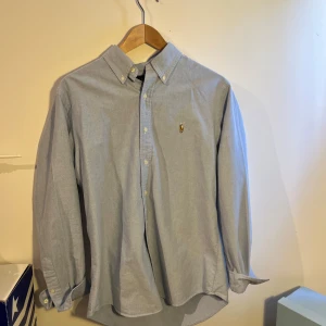 Ljusblå skjorta från Ralph Lauren - Klassisk ljusblå skjorta från Ralph Lauren med button-down krage och broderad logga på bröstet. Skjortan har lång ärm, custom fit och är tillverkad i mjuk bomull. Perfekt för en clean och stilren look.