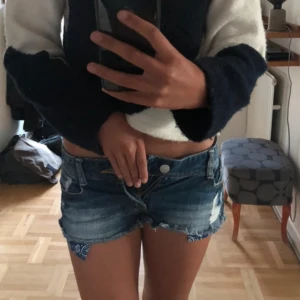 Blå slitna jeansshorts  - Snygga blå jeansshorts från Six Denim Collection med slitna detaljer och fransig kant. Lågmidjade och med klassiska fickor både fram och bak. Perfekta för sommaren och ger en cool, avslappnad vibe.