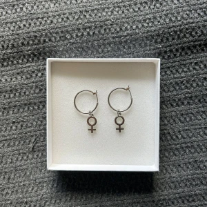 Silvriga örhängen med venus-symbol - Snygga silvriga hoops med hängande venus-symboler. Perfekta för dig som vill ha ett statement-smycke.