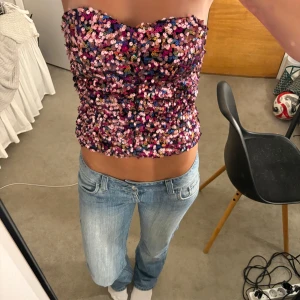 Paljettprydd tubtopp från Zara - Glittrig tubtopp från Zara täckt av paljetter i rosa, lila, guld och svart. Bandeau-modell med hjärtformad överkant och figurnära passform. Perfekt för att sticka ut och skapa en färgstark look. Fodrad insida för extra komfort.