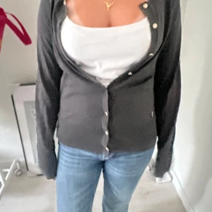 Mörkgrå kofta med knappar - Snygg mörkgrå kofta med långa ärmar och klassisk rund halsringning. Koftan har stilrena knappar framtill och är perfekt att slänga över ett linne eller t-shirt. Enkel och tidlös design som passar till jeans eller kjol.