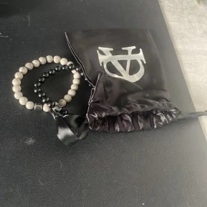 Två pärlarmband från Allcap one - Säljer två snygga pärlarmband från Allcap one. Ett armband är helsvart med blanka pärlor, det andra är grått med marmorerade pärlor. Båda har en cool, minimalistisk vibe och levereras i en svart satinpåse med logga.