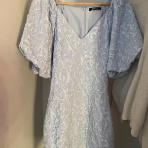 Ljusblå kort puffärmad klänning Gina Tricot - Supersöt ljusblå kort klänning från Gina Tricot med puffiga korta ärmar och v-ringning. Klänningen har ett blommigt strukturmönster i tyget och dragkedja bak. Bara använd en gång och storlek 34/Xs Skriv privat för mer frågor💗