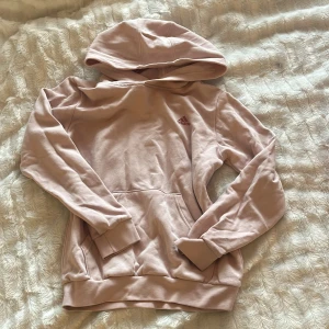 Ljusrosa hoodie - Säljer en ljusrosa hoodie från Adidas med klassisk logga på bröstet. Tröjan har huva, magficka och långa ärmar med muddar. Mjuk och skön i bomullsmix, perfekt för chill dagar eller när du vill ha en enkel och snygg look.