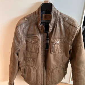 Jofama skinnjacka – Klassisk bikerstil i äkta läder, herr, storlek S/M - Japan inspirerad skinnjacka från välkända Jofama – ett svenskt märke känt för hög kvalitet och tidlös design. Jackan är tillverkad i äkta läder med ett snyggt, slitet uttryck som bara blir bättre med tiden. Perfekt för dig som vill ha en robust och stilren bikerinspirerad look som fungerar både till vardags och vid speciella tillfällen.