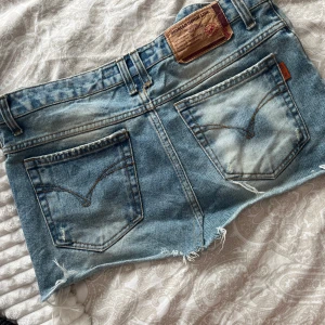 Blå jeanskjol från Ingalls Jeans - Snygg ljusblå jeanskjol från Ingalls Jeans med slitna detaljer och råa kanter. Klassisk femficksmodell, normal passform och cool tvätt. Perfekta för varma dagar och en avslappnad stil. Midjemått 38cm. Inköpt för 499-:🥰 använt skick 