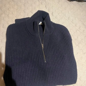 Mörkblå stickad half zip-tröja FILIPPA K - Säljer en mörkblå stickad tröja från FILIPPA K med ribbad struktur och half zip-dragkedja. Tröjan har hög krage och långa ärmar, perfekt för kyliga dagar. Enkel och stilren design som funkar till det mesta. 7.5/10 finns ett litet hål under ärmen som kan behöva lagas  retail 2400kr heavy knit
