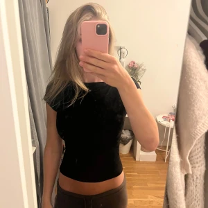 Svart croppad topp med öppen rygg - Säljer en svart croppad topp med korta ärmar och en snygg öppen rygg. Toppen har en tight passform och är tillverkad i mjuk bomull, perfekt för dig som gillar minimalistisk stil med en twist. Enkel att matcha med både jeans och kjol.