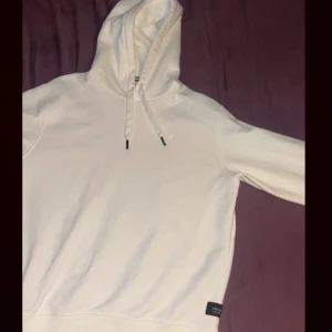 Vit hoodie från Replay med huva - Snygg vit hoodie från Replay med klassisk huva och snörning. Tröjan har en liten broderad logga på bröstet och en svart Replay-lapp nertill. Mjuk insida och ribbade muddar. Perfekt för en clean och stilren look.