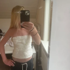 Vit bandeau tubtopp från Bik Bok - Superfin vit bandeau tubtopp från Bik Bok med 3D-blommiga spetsdetaljer över hela toppen. Toppen är axelbandslös och har en tight passform som sitter snyggt. Perfekt för dig som vill sticka ut med en romantisk och trendig look 💘
