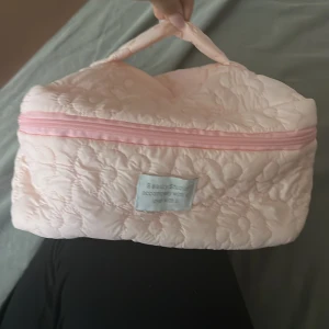 Quiltad ljusrosa väska med blommor - Supersöt quiltad väska i ljusrosa med blommigt mönster och matchande dragkedja. Perfekt storlek för smink eller småprylar, med ett mjukt handtag upptill. Materialet är syntet och väskan har en charmig vibe.