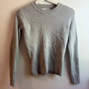 Grå ribbad långärmad tröja Zara - Säljer en stilren grå ribbad långärmad tröja från Zara. Tröjan har rund halsringning och är figurnära i modellen, perfekt för lager-på-lager. Materialet är mjukt och stretchigt för en bekväm känsla hela dagen.