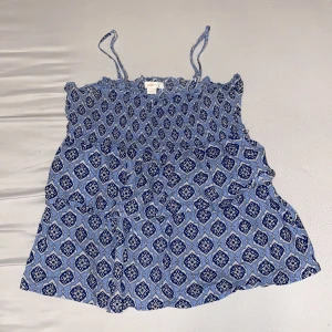 Blå mönstrad linnetopp från Gina Tricot - Supersöt blå linnetopp från Gina Tricot med smala axelband och ett unikt vitt och mörkblått mönster. Toppen har smock upptill och är luftig med flowy passform, perfekt för varma dagar. Materialet känns mjukt och lätt mot huden.