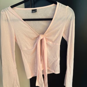 Ljusrosa topp från Gina Tricot - ljusrosa topp från Gina Tricot med långa ärmar och knyt framtill. Tunn i materialet. Bra skick men nopprig vid brösten och armarna 