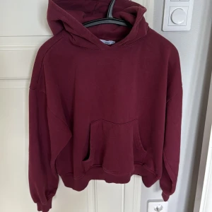 Mörkröd hoodie med huva  - Enkel och snygg mörkröd hoodie med huva och stor magficka. Modellen är loose fit med långa ärmar och ribbade muddar. Perfekt för chill dagar eller när du vill ha något bekvämt och stilrent. Materialet är mjuk bomullsmix.