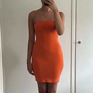 Orange tubklänning i tight modell - Säljer en snygg orange tubklänning i tight passform. Klänningen är axelbandslös och kort, perfekt för dig som vill sticka ut. Enkel och stilren design utan mönster, passar dig som gillar färg. 