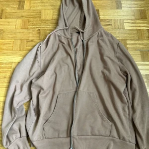 Beige hoodie med dragkedja - Enkel beige hoodie med dragkedja och huva. Tröjan har två stora fickor framtill och ribbade muddar vid ärmslut och nederkant. Mjuk insida som känns skön mot huden. Perfekt för chill dagar eller när du vill ha något bekvämt.