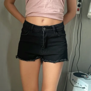 Svarta jeansshorts från Shein Teen - Svarta jeansshorts från Shein Teen med hög midja och råa, fransiga kanter. Klassisk femficksmodell med knapp och dragkedja framtill. Snygg och enkel design som passar perfekt till sommaren.