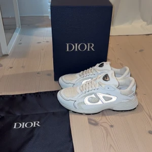 Vita Dior B30 sneakers - Säljer dessa extremt snygga dior B30 skor helt oanvända 10/10 skick!! Perfekt skor nu fram till hösten. Dior loggan är en reflex så när man lyser på dem så lyser dem till😊✅