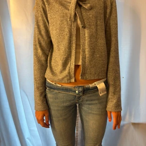 Grå croppad kofta med knyt - Superfin gråmelerad kofta med croppad passform och knyt framtill. Långärmad och mjuk, perfekt att slänga över ett linne eller topp. Enkel och stilren design som funkar till jeans eller kjol.