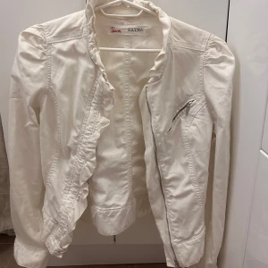 Vit jeansjacka med volang - Snygg vit jeansjacka med volangdetaljer  och axlar med lätt puff. Mycket fint skick. Kontakta för fler bilder. Pris går att diskutera.