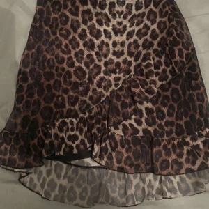 Leopardmönstrad volangkjol - Säljer en kort kjol med leopardmönster och volangdetaljer. Kjolen har bruna och svarta toner och är tillverkad i ett lätt, transparent material som ger en snygg och luftig känsla. Perfekt för dig som vill sticka ut med en trendig look.