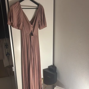 Balklänning rosa  - Säljer en långklänning i dusty rosa med v-ringning,  vida ärmar och snygg omlott-detalj framtill. Klänningen har uringing under bysten och är gjord i ett mjukt, flowy material som faller snyggt. Använd en gång