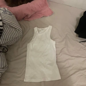 Vit ribbad linnetopp från Weekday - Säljer en klassisk vit ribbad linnetopp från Weekday. Modellen är ärmlös med rund halsringning och tight passform, perfekt för lager-på-lager eller sommarens alla outfits.