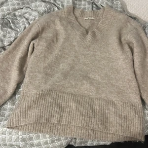 Beige stickad v-ringad tröja Gina Tricot - Mysig beige stickad tröja från Gina Tricot i v-ringad modell. Tröjan har bred ribbstickad kant nedtill och vid ärmslut, samt lång ärm. Perfekt för lager-på-lager och chill dagar.