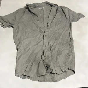 Olivgrön linneskjorta från Cubus, S - Säljer en grå kortärmad skjorta från Cubus i blandning av linne och bomull. Skjortan har klassisk krage, knäppning framtill och en avslappnad regular fit. Perfekt för varmare dagar och enkel att styla till jeans eller shorts.