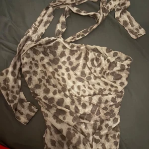 Leopardmönstrad bandeau topp med knyt - Säljer en leopardmönstrad bandeau topp med knyt runt halsen. Toppen är croppad och har en tight passform som framhäver midjan. Perfekt för dig som vill sticka ut med ett djurmönster och trendig look.