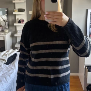 Svart och beige randig stickad tröja - Säljer en svart stickad tröja med breda beigea ränder. Tröjan har en rund halsringning och är långärmad med en relaxed fit. Perfekt för dig som gillar en chill och stilren look. Passar både till jeans och kjol för en enkel men snygg outfit.