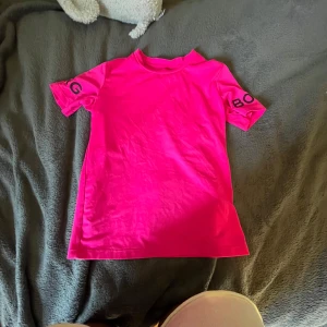 Neonrosa träningströja från Björn Borg - Säljer en neonrosa t-shirt från Björn Borg med tryck på båda ärmarna. T-shirten har klassisk passform, rund hals och är tillverkad i mjukt bomullstyg. Perfekt för dig som vill sticka ut med en färgstark look.