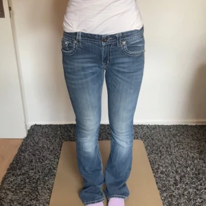 Miss me Blå Miss Me jeans med blingade fickor - Säljer ett par blå jeans från Miss Me med snyggt slitna detaljer och blingade bakfickor med paljetter och nitar. Jeansen har normal passform, låg midja och utsvängda ben. Perfekta om du gillar statement-detaljer och vill sticka ut lite extra. En knapp är utbytt som man ser