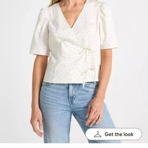 Vit omlottblus med prickigt mönster - Snygg vit omlottblus med svarta prickar och korta puffärmar. Blusen har v-ringning och knytband i sidan. Aldrig använd då jag ångrar köpet, dock e prislappen av. 