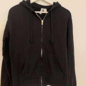 Svart hoodie med dragkedja - Svart hoodie från H&M i storlek XS. Klassisk modell med huva, snörning och dragkedja framtill. Mjuk bomullsblandning och två stora fickor framtill. 