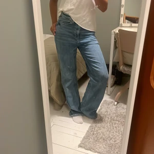 Blåa wide jeans med hög midja - Säljer ett par blåa jeans med hög midja och wide fit. Klassisk femficksmodell med dragkedja och knapp framtill. Jeansen har en avslappnad passform och raka, vida ben. Perfekta för en chill och trendig look.