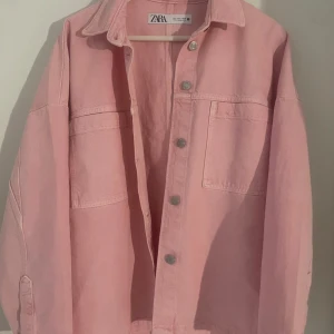 Rosa jeansjacka från Zara - Säljer en ljusrosa jeansjacka från Zara med stora bröstfickor och silvriga knappar framtill. Jackan har klassisk krage och långa ärmar med knapp vid ärmslut. Perfekt för att addera färg till din outfit!