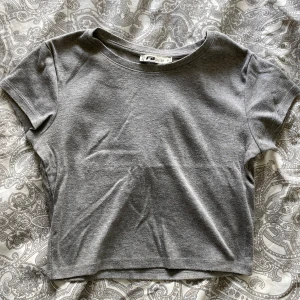 Grå croppad t-shirt från FB Sister - En enkel och stilren grå croppad t-shirt från FB Sister. T-shirten har korta ärmar och rund halsringning, perfekt för en avslappnad look.