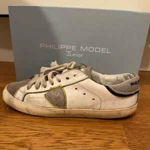 Philippe Model Junior vita och grå sneakers - Säljer ett par Philippe Model Junior sneakers i vitt och grått med svarta och limegröna detaljer.  Skorna är ej tvättade och skosnörerna går att fixa nya. Box och kvitto finns 