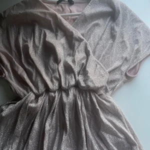 Ljusrosa glittrig omlottklänning från Bik Bok - Supersnygg ljusrosa omlottklänning från Bik Bok med glittrigt tyg och resår i midjan. Klänningen har korta ärmar och ett fint fall. Perfekt för dig som vill sticka ut med lite extra glitter.