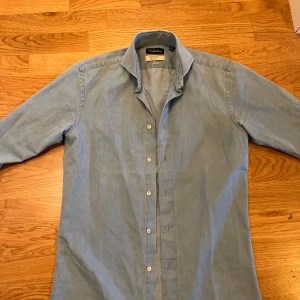 Oscar Jacobson - Säljer en ljusblå skjorta från Oscar Jacobson. Skjortan har klassisk krage, knäppning framtill och är i slim fit. Perfekt för dig som gillar stilrena och enkla plagg. Hör av dig vid frågor.