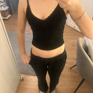 Svart ribbad linnetopp med spets från Bik Bok - Svart croppad linnetopp från Bik Bok med smala axelband och fina spetsdetaljer längs urringningen. Toppen är ribbad och har en figurnära passform, perfekt att styla till olika outfits. Använd fåtal gånger.