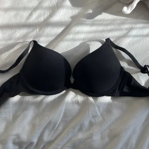Svart push-up bh från Dorina - Säljer en svart push-up bh från Dorina med släta kupor och justerbara axelband. Bh:n har en enkel och stilren design, perfekt under alla typer av toppar. Stängs med hyskor bak.